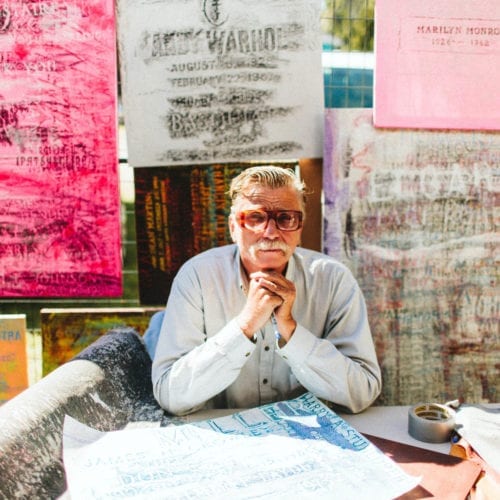 An artist seated in front of grave rubbings at Outsiders Outside Art Fair in Harbert, Michigan.