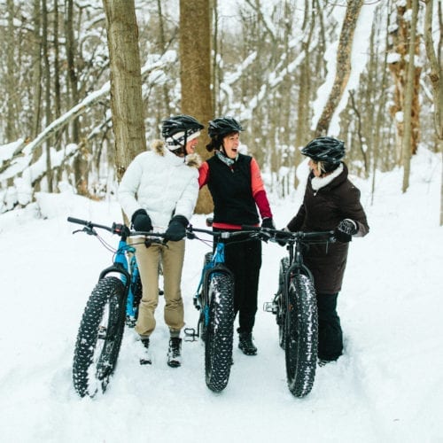 Three women laughing with their fat tire snow bikes at Love Creek County Park in southwest Michigan.