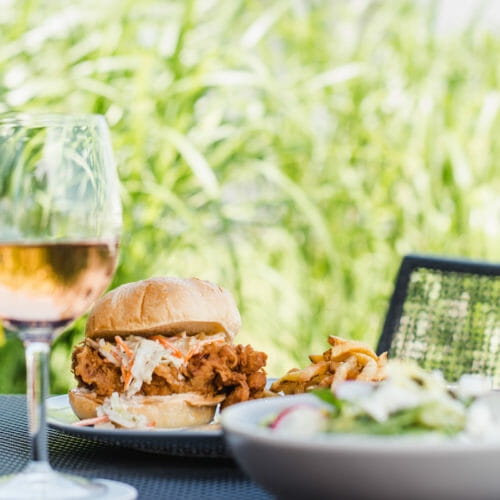 Spicy Korean fried chicken sandwich in front of a dune-grass backdrop on the patio at Bentwood Tavern in New Buffalo, Michigan.