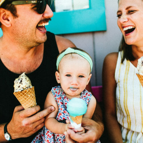 A young couple laughing as their baby tries ice cream for the first time at Oink's Dutch Treat in New Buffalo, Michigan.