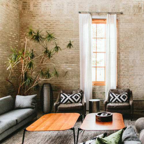 Living room with high ceilings, brick walls, two dark leather chairs, upholstered sofa and large houseplant at The Flat at Journeyman Distillery in Three Oaks, Michigan.