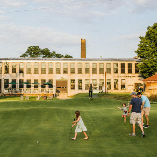 A family playing Welter's Folly putting green with Journeyman Distillery in the background in Three Oaks, Michigan.