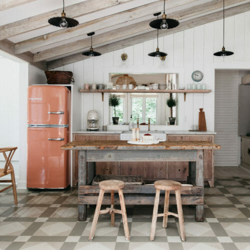 Kitchen with salmon-colored refrigerator, vaulted whitewashed wood ceiling, primitive island and geometric floor tile at The Leo Cottage in New Buffalo, Michigan.