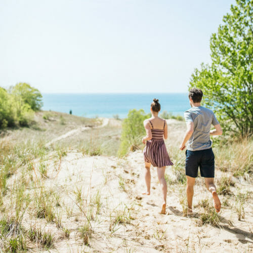 Couple frolicking on the sand dunes with a view of Lake Michigan at Warren Dunes State Park in Sawyer, Michigan.
