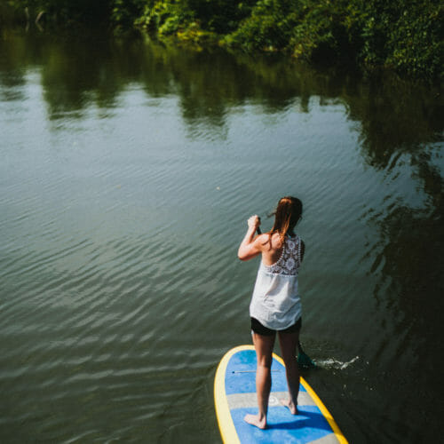 A young woman in a flowered white tank top and brown ponytail paddling the Galien River Marsh Trail in New Buffalo, Michigan.