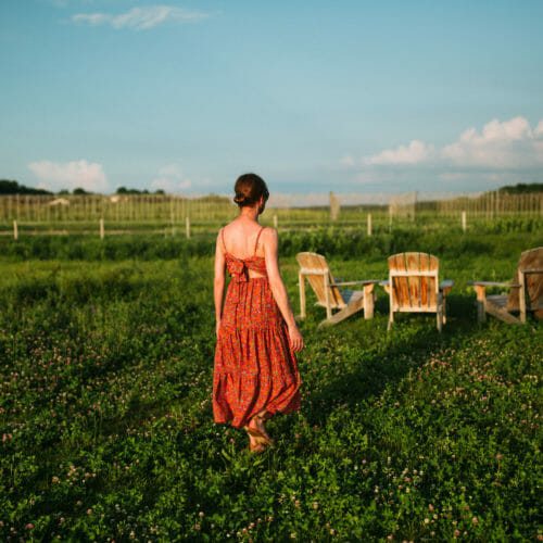 A woman in an orange sundress walking across a grassy field at River Saint Joe brewery in Buchanan, Michigan.