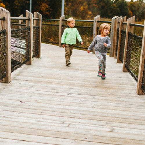 Two small children running down the elevated walkway at Galien River County Park in New Buffalo, Michigan.