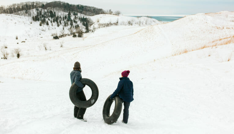 A couple with inner tube sleds looking down a steep lakefront dune at Warren Dunes State Park in Sawyer, Michigan.
