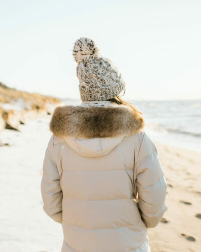 A women in a white parka and warm hat on the beach at Warren Dunes State Park in Sawyer, Michigan.