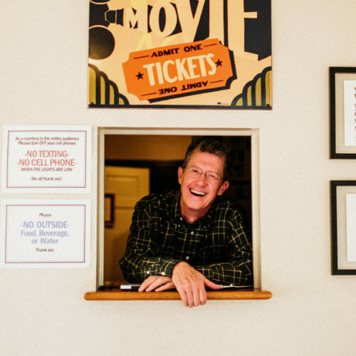 Owner Bill Lindblom smiles in the ticket window of Vickers Theatre in Three Oaks, Michigan.