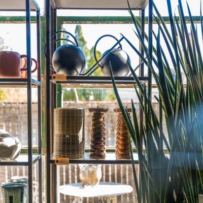 Sunlight spill through a large window behind a display of plants, watering cans, and planters at Alapash Mercantile in Three Oaks, Michigan.