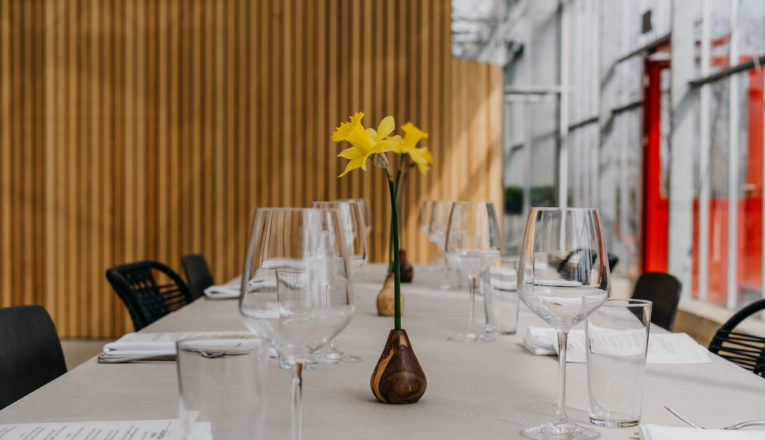 A long table set with wine glasses and daffodils in front of a modern wood wall at Granor Farm in Three Oaks, Michigan.