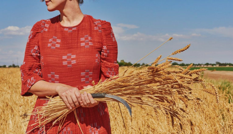 Emma Zimmerman in a red textured dress in front of a holden wheat field.