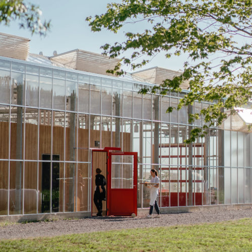 A stately, glass greenhouse with red doors and interior wood volumes at Granor Farm in Three Oaks, Michigan.