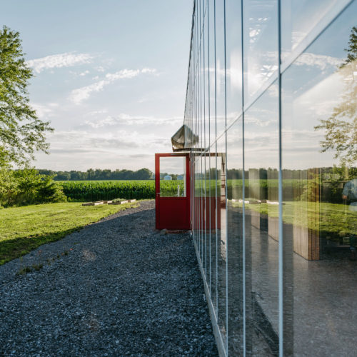A view past a glass greenhouse with red door to fields at Granor Farm in Three Oaks, Michigan.