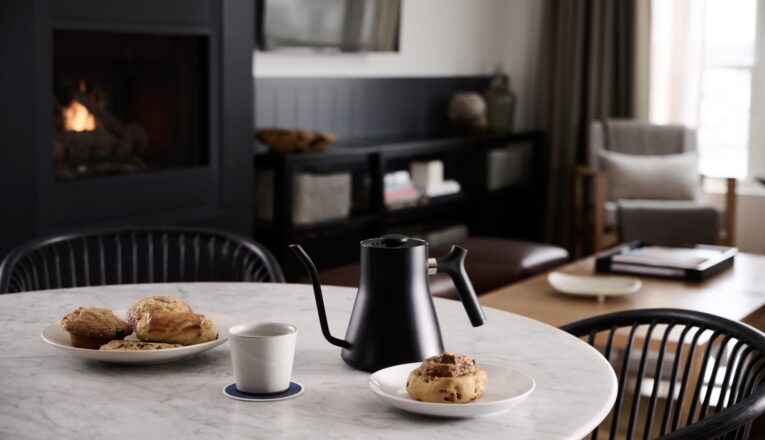 A black water kettle and scones on a marble tabletop with a black fireplace in the background at Marina Grand Resort in New Buffalo, Michigan.
