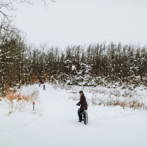 A woman riding a fat tire bike looks back before entering a snowy forest path at Love Creek County Park in southwest Michigan.