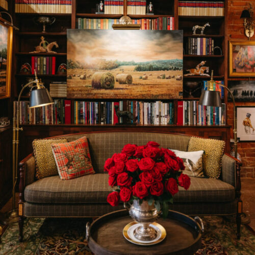 Various framed paintings hang on a wall behind a couch and a bouquet of red roses during Art Attack in New Buffalo, Michigan.