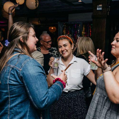 Three women enjoy drinks and conversation on the dance floor at the Harbor Country Pride Prom event in Union Pier, Michigan.