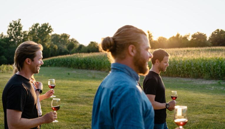 Three young men holding a glass of red wine as they walk the vineyard at Hickory Creek Winery in Buchanan, Michigan.