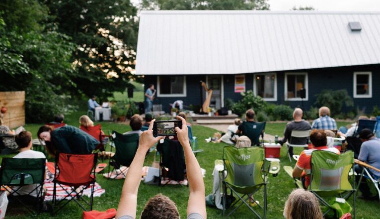 People sitting in a rural yard watching live music performed on a porch in Galien, Michigan.