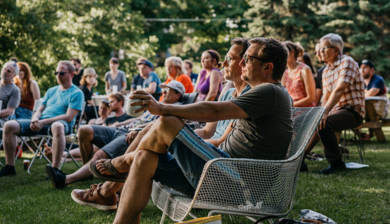 An audience on a grassy lawn watches a performance at The Storehouse in New Buffalo, Michigan.