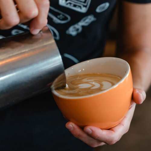A barista artfully pours a latte into an orange mug at Infusco Coffee Roasters in Sawyer, Michigan.