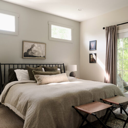 A bright bedroom with neutral decor and large windows.