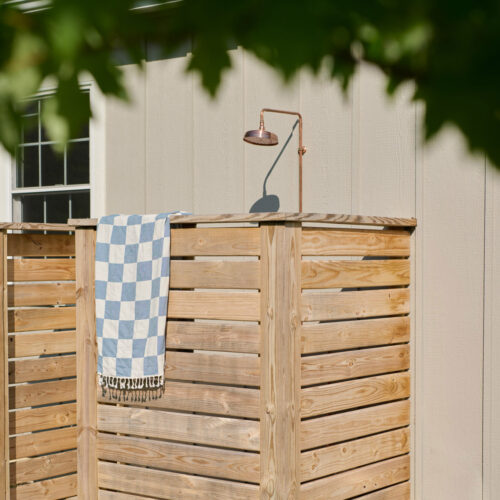 A blue-checked towel drapes over the wooden privacy wall of an outdoor shower at Wandering Soul Cabin in Sawyer, Michigan.