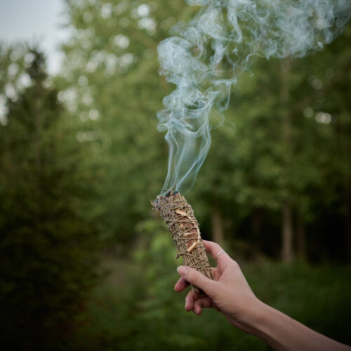 A guest's hand waves a smoldering bundle of sage outside near the fire pit at Wandering Soul Cabin in Sawyer, Michigan.