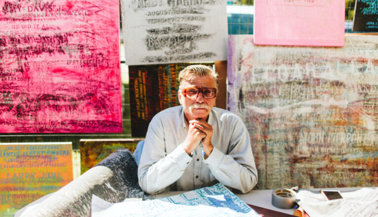 An artist seated in front of grave rubbings at Outsiders Outside Art Fair in Harbert, Michigan.