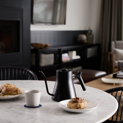 Sleek black water kettle and pastries on a white marble table with a black firelace in the background in a suite at Marina Grand in New Buffalo, Michigan.