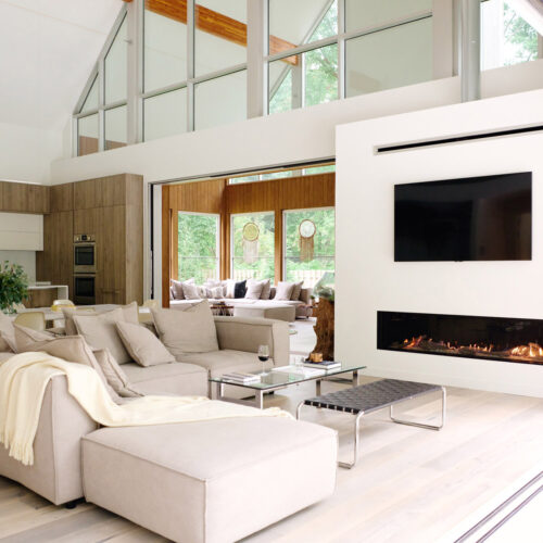 A soaring, sun drenched living room with modern furnishings and a wood burning fireplace at Sol Haus in Union Pier, Michigan.