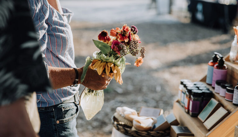 A close-up of a woman holding a bouquet of flowers while browsing a market stand at New Buffalo Farmers Market in New Buffalo, Michigan.