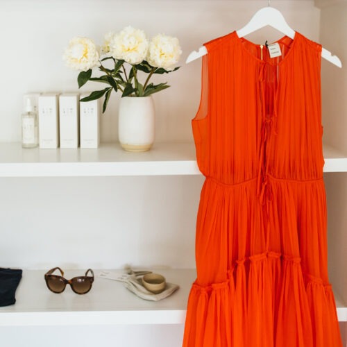 A gauzy orange dress hangs in front of white shelves styled with black and white accessories at AP Shops in Lakeside, Michigan.