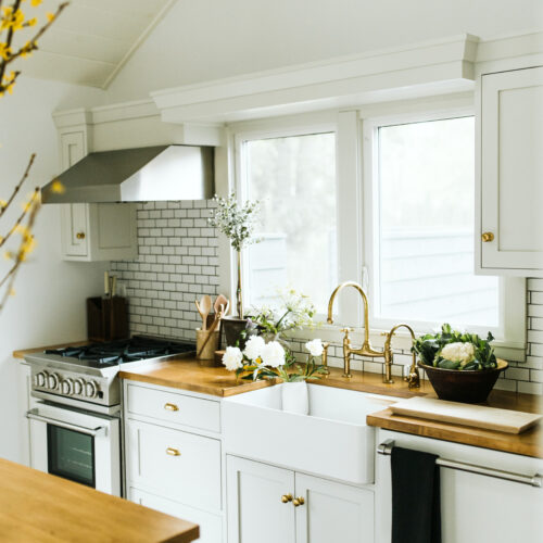 A bright white kitchen with subway tiles, warm wood counters, and fresh flowers sitting in the sink at Shamrock House in Harbert, Michigan.