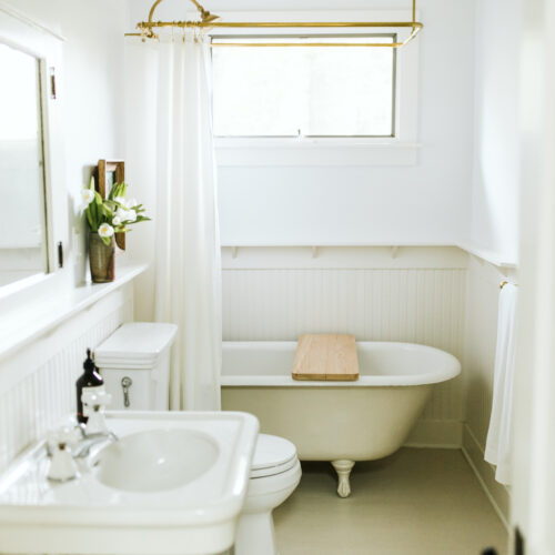 A white-washed bathroom with a pedestal sink and claw-foot tub at Shamrock House in Harbert, Michigan.