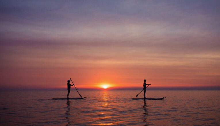 Two young women paddleboard along the horizon as the sun sets over Lake Michigan in New Buffalo.