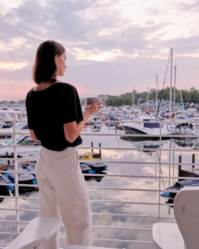 A young woman with a mug of coffee looks out onto the boats in New Buffalo harbor.