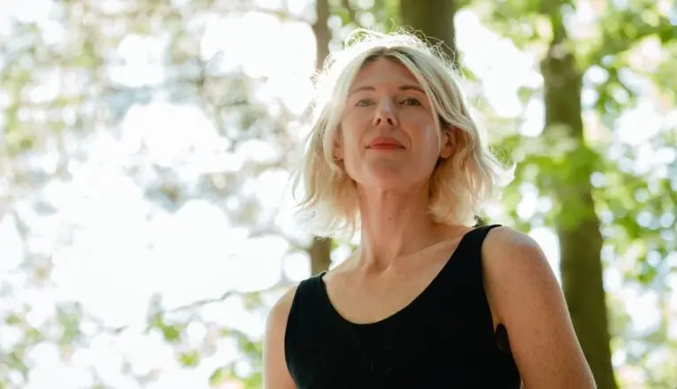 Indie rocker Rosali gazes at the camera in front of a grove of trees.