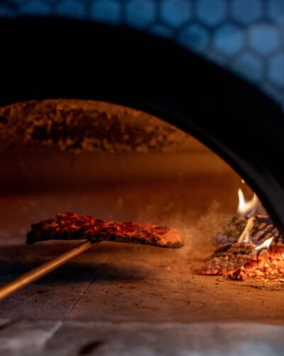 A steaming pizza being pulled out of a wood-fire oven on a wood pizza peel at Emma Hearth & Market in Bridgman, Michigan.