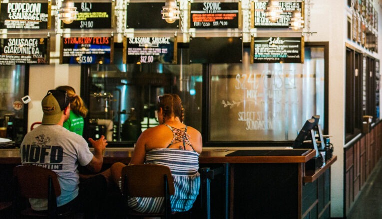 A couple sits at the bar underneath the handwritten pizza, food, and beer menus at Haymarket Brewery and Taproom in Bridgman, Michigan.