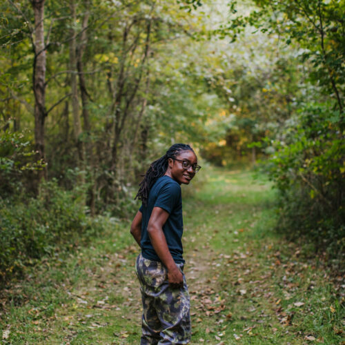 A woman looking back over her shoulder on a grassy trail in the woods.