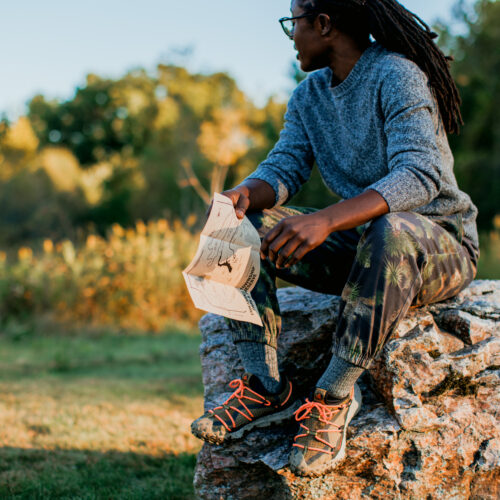 A woman sitting on a rock holding a trail map looking out onto prairie and trees.
