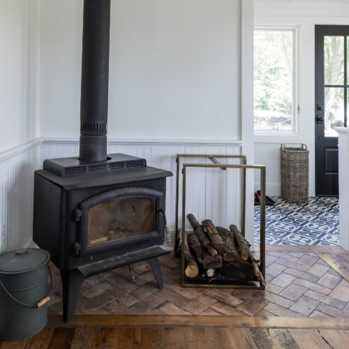 An old wood-burning stove next to extra firewood in a living room.