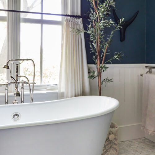 A large soaking tub in front of a window in a dark blue bathroom.