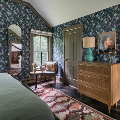 A bedroom with dark blue wallpaper and high ceilings decorated with vintage furniture and eclectic art.