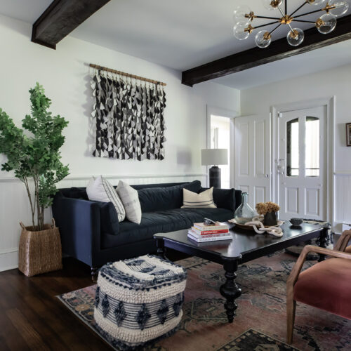 A bright living area with white walls, dark beams, dark hard woods floors, and plenty of furniture with various textures.