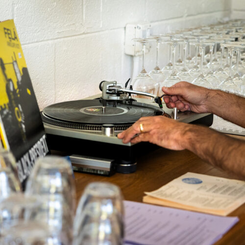 A man starts playing a record next to a record collection and glassware.