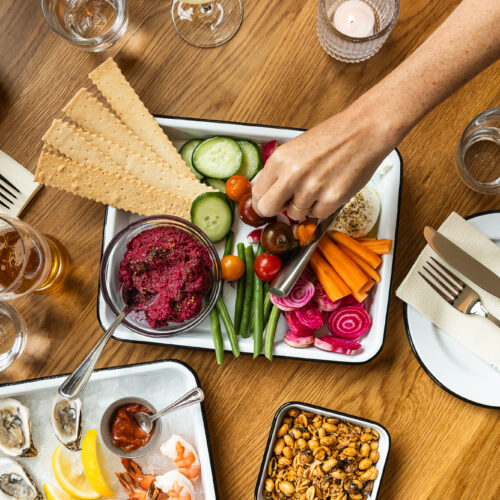 A hand reaches for fresh vegetables over a spread of colorful dishes.
